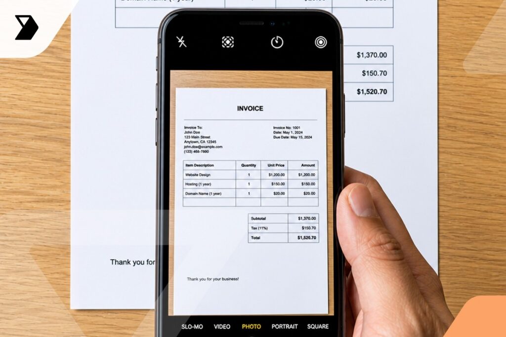 A hand holds a smartphone taking a photo of an invoice document on a table.