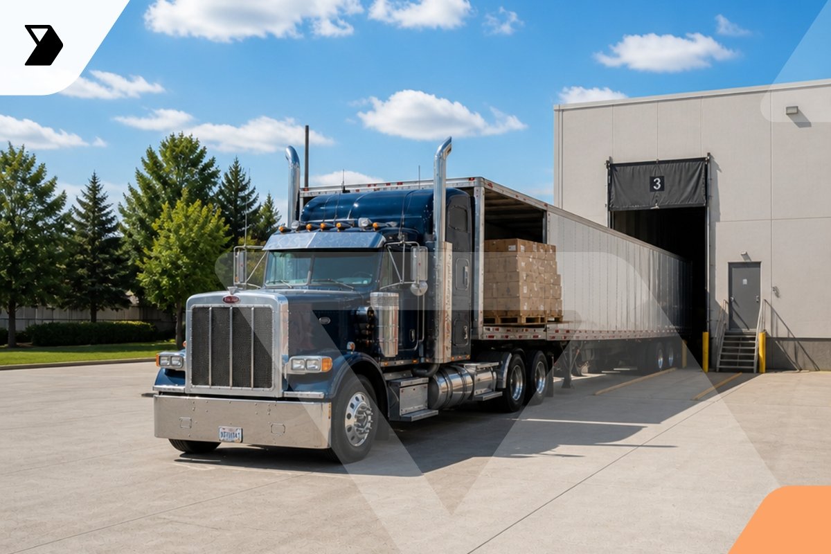 A large blue semi-truck is backed up to a loading dock at a warehouse.
