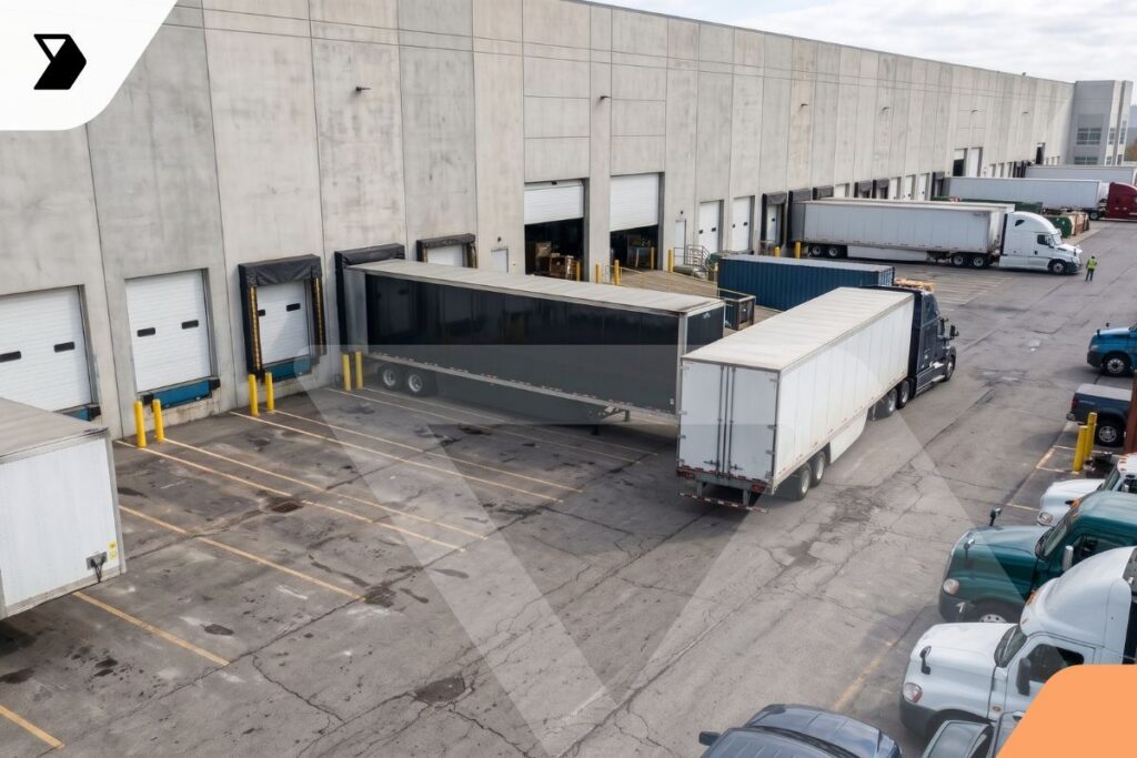 High-angle view of semi-truck trailers parked at the loading docks of a large concrete warehouse.